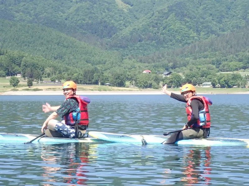 Two people sitting on their SUPs and waving, enjoying a relaxing and fun tour on the calm lake.