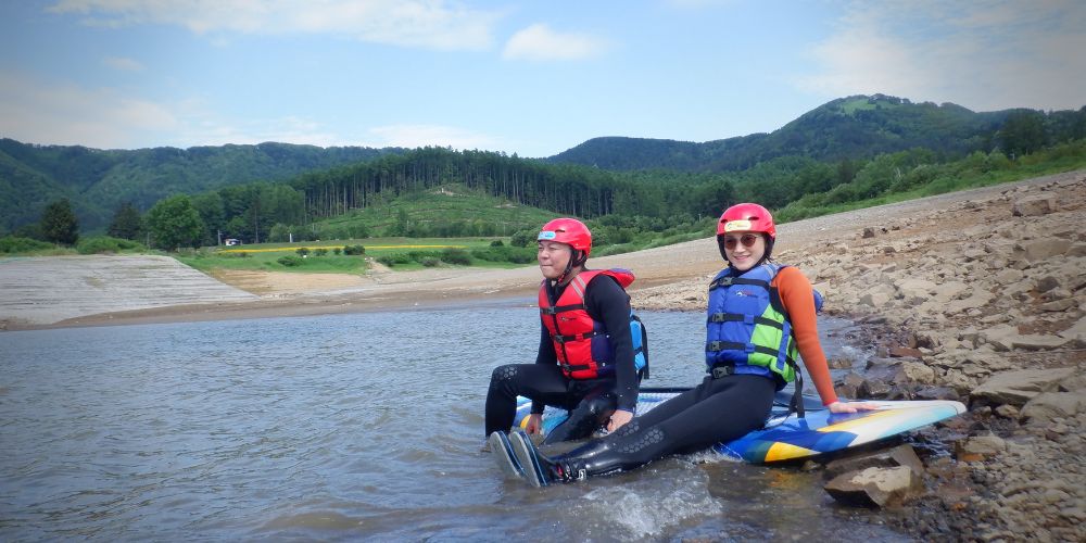 Two participants sitting on the edge of their paddleboards, getting used to the water temperature before launching.