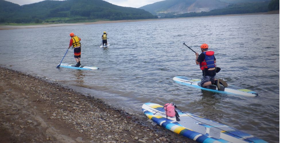 A group of SUP paddlers heading out from the shore onto the vast expanse of Lake Kanayama.