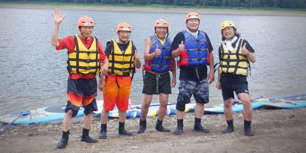 A group of five smiling participants posing for a photo on the shore of Lake Kanayama after their tour.