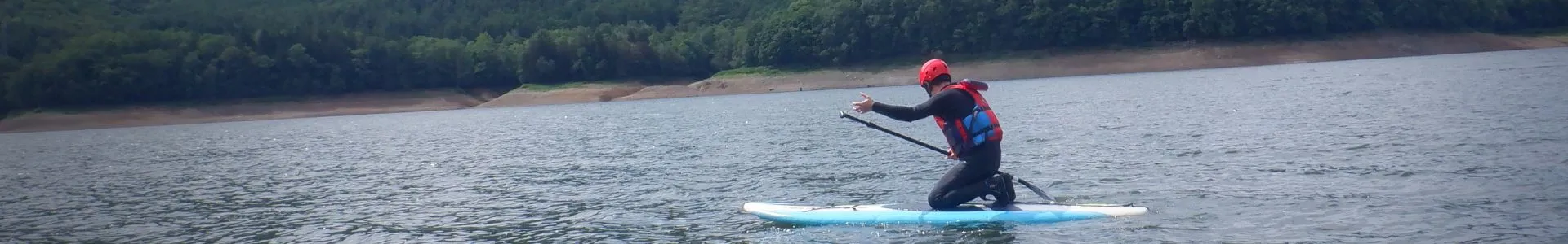 A participant giving a thumbs-up while kneeling on a paddleboard on the vast, scenic Lake Kanayama.