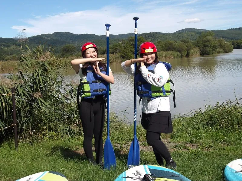 Two participants having fun and making a playful pose with their paddles on the grassy shore of Lake Nokanan.