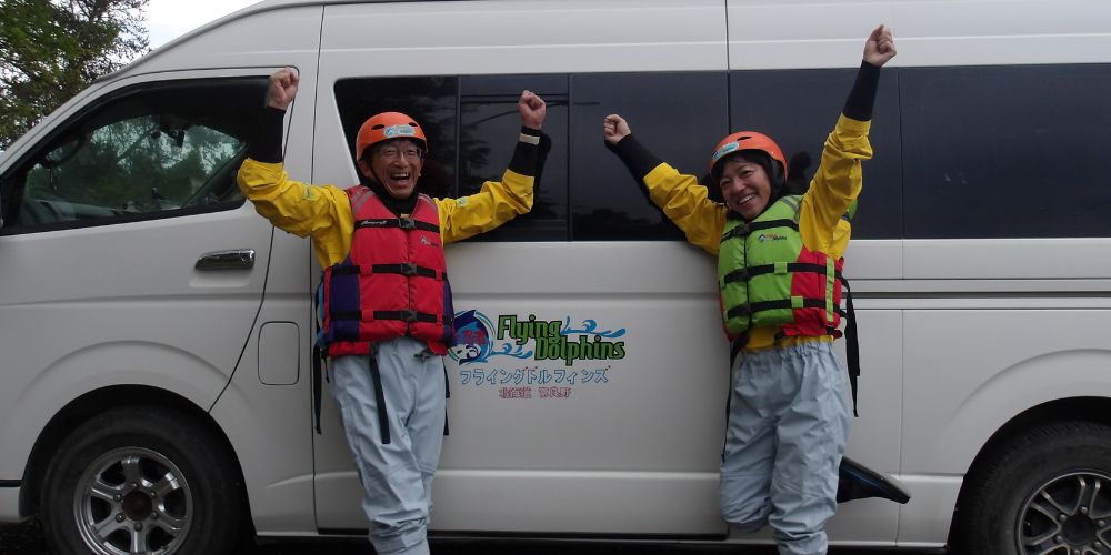 Two participants posing with their paddles and SUP boards on the shore while receiving a basic lesson from the guide.