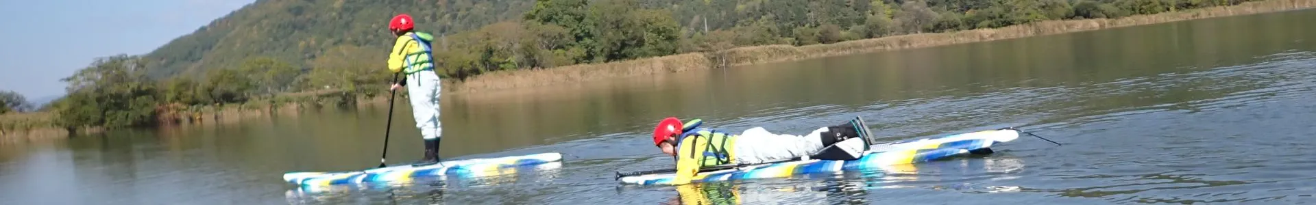 Two people enjoying a peaceful Stand Up Paddleboard tour on the calm waters of Lake Nokanan, surrounded by beautiful green mountains.