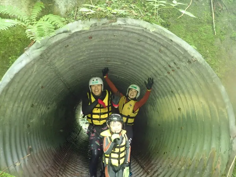 A family having fun and posing inside a large tunnel, one of the unique features of the Tonashibetsu canyoning course.
