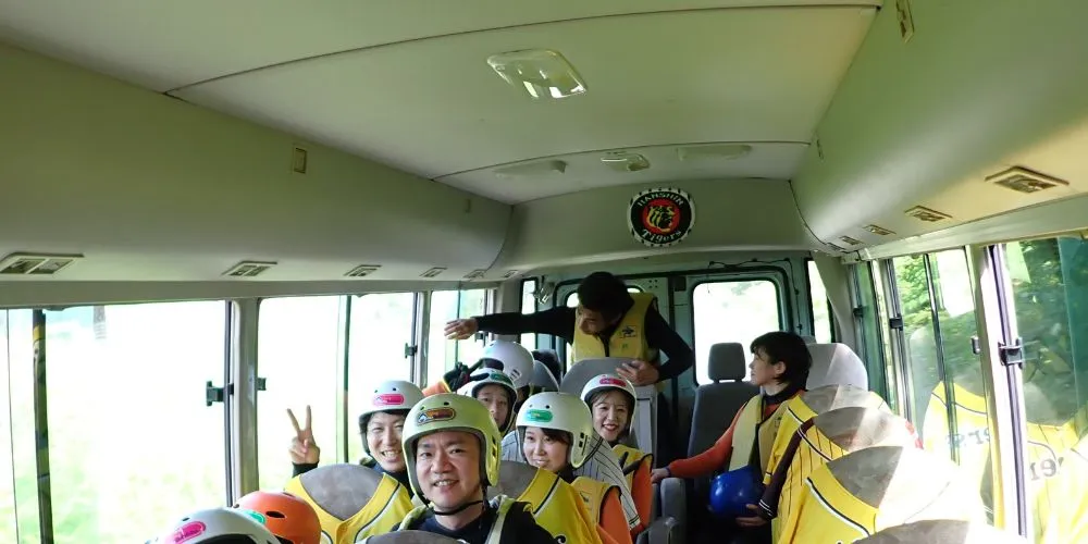 A group of smiling participants in full canyoning gear, excited for the adventure inside the transfer bus.