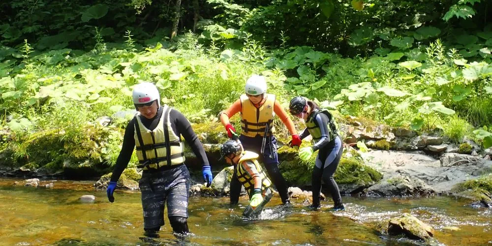 A guide helping a family as they take their first steps into the shallow, clear water of the Tonashibetsu canyon.