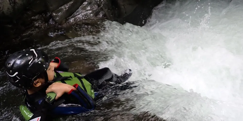 A child enjoying the thrill of a natural waterslide, splashing into the water during the canyoning tour.