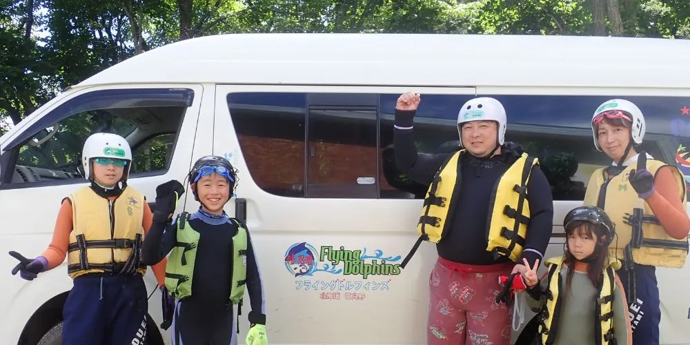 A happy family posing with their guide in front of the van after successfully completing the canyoning adventure.