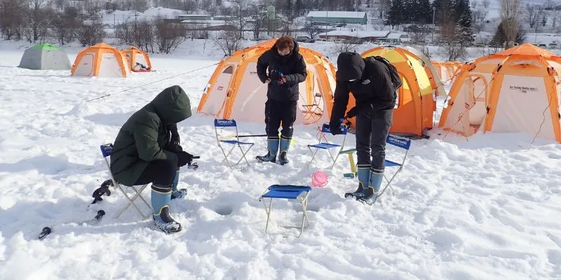 A large group of tourists posing for a photo on the frozen lake, ready for their ice fishing adventure.
