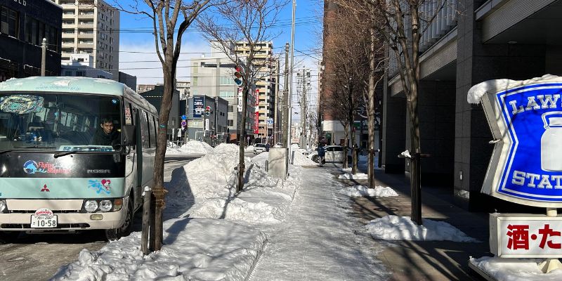 The Flying Dolphins shuttle bus parked on a snowy street in Sapporo, near a Lawson convenience store.