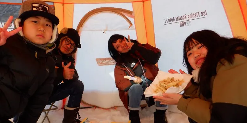 A happy family of three making peace signs while comfortably fishing inside a bright orange tent.